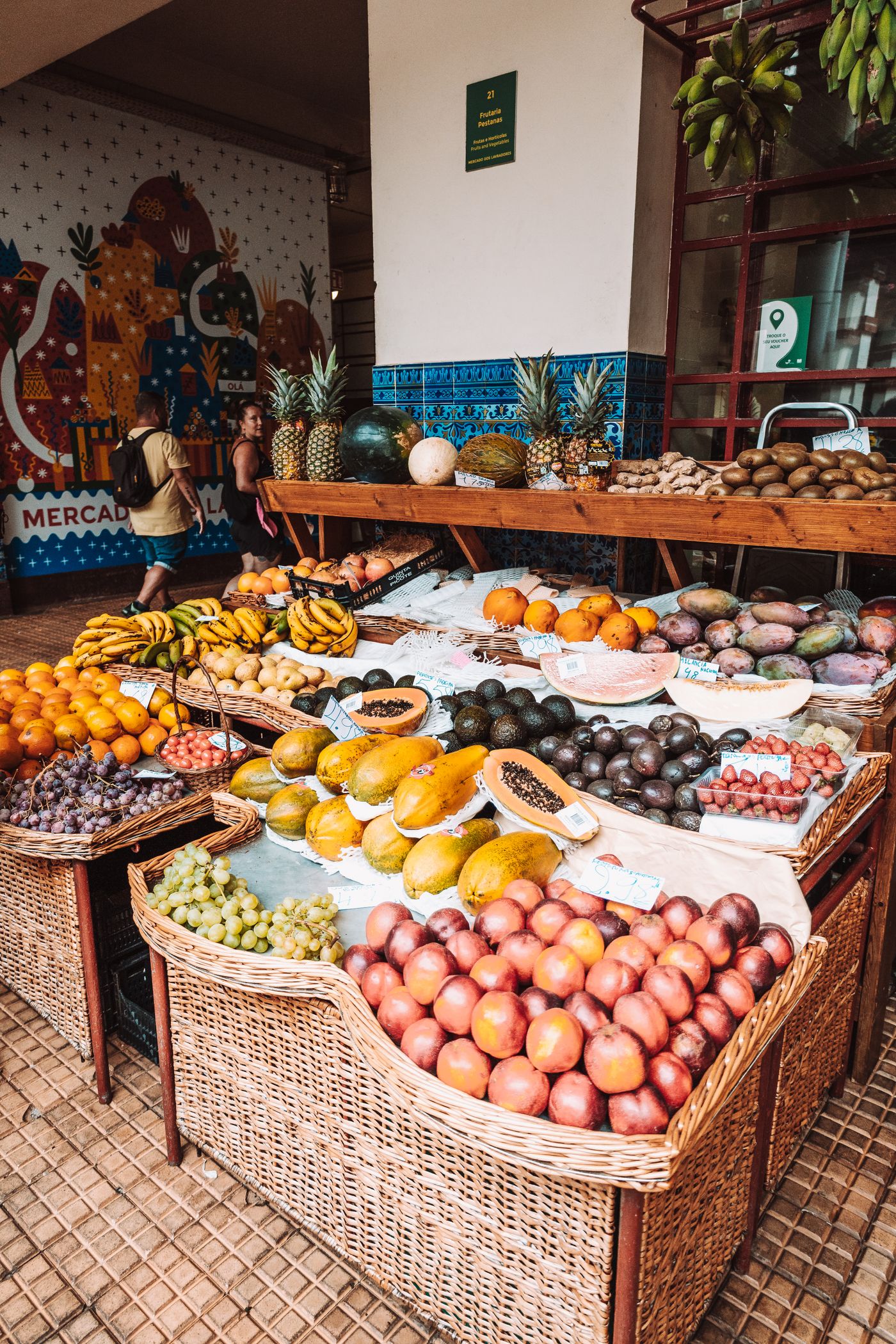 Exotic-fruit stall at Mercado dos Lavradores with custard apple, passionfruit and bananas in wicker baskets, the Mercado mural behind