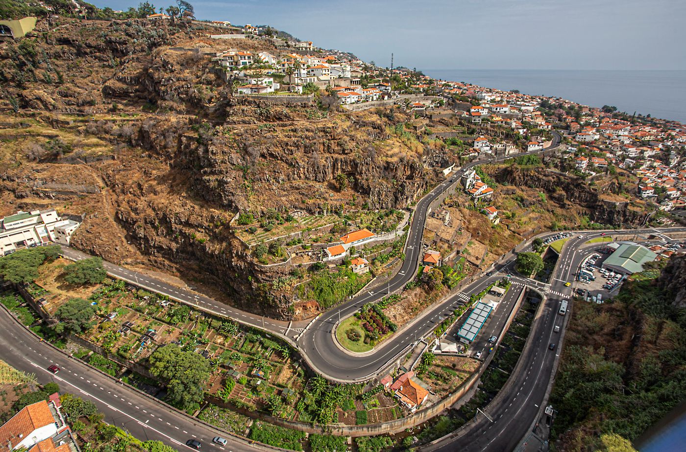 Aerial view of switchback hairpin roads zigzagging down a cliff toward the sea on Madeira's south coast