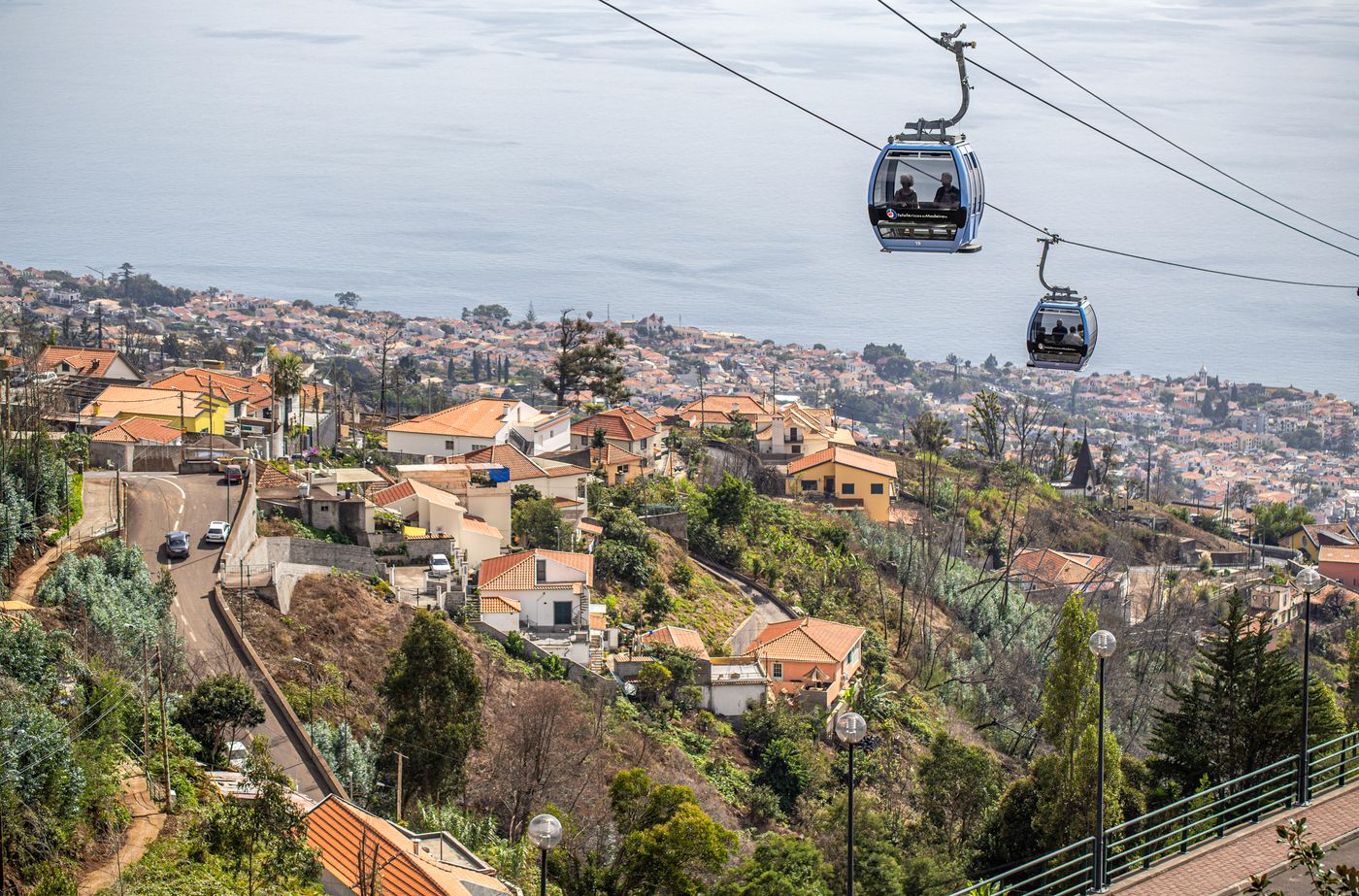 Two cable car gondolas over the terracotta rooftops of Funchal with the bay and ocean behind