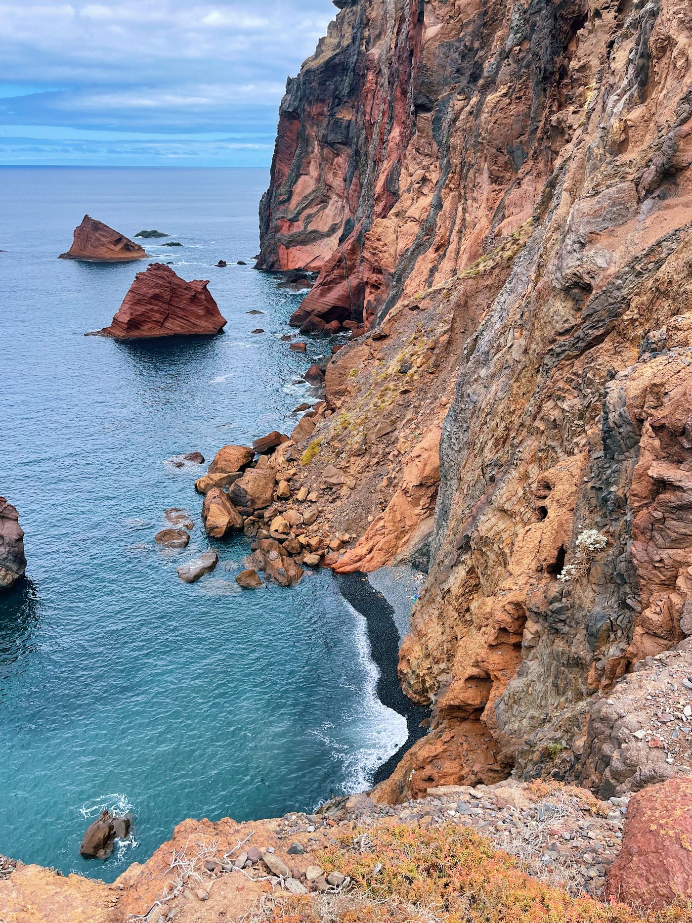 Red and ochre banded volcanic sea cliffs at Ponta de São Lourenço with a detached red sea stack standing in turquoise water