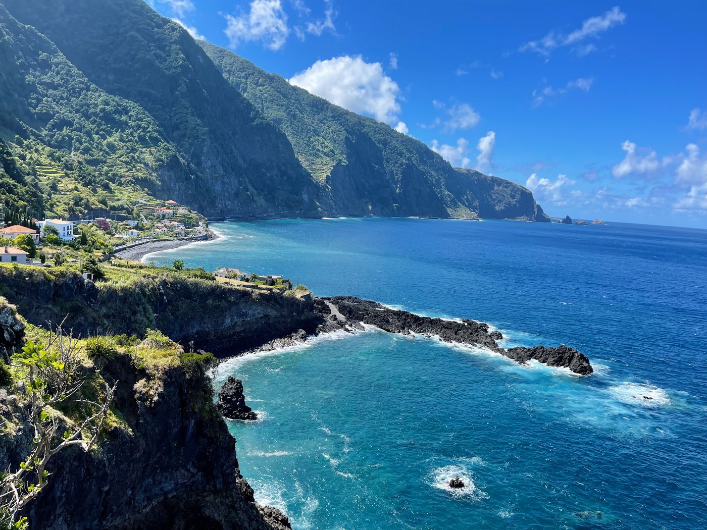 Green cliffs dropping to the sea at Seixal on Madeira's north coast, with white houses and a dark beach below the mountains