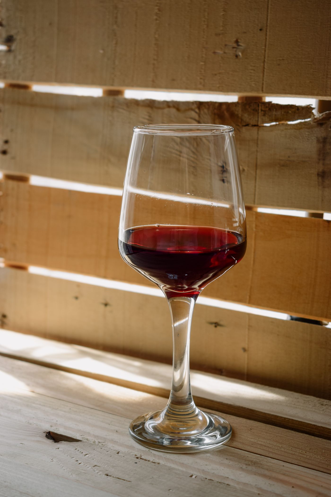 A glass of red wine catching the afternoon light on a rustic wooden table